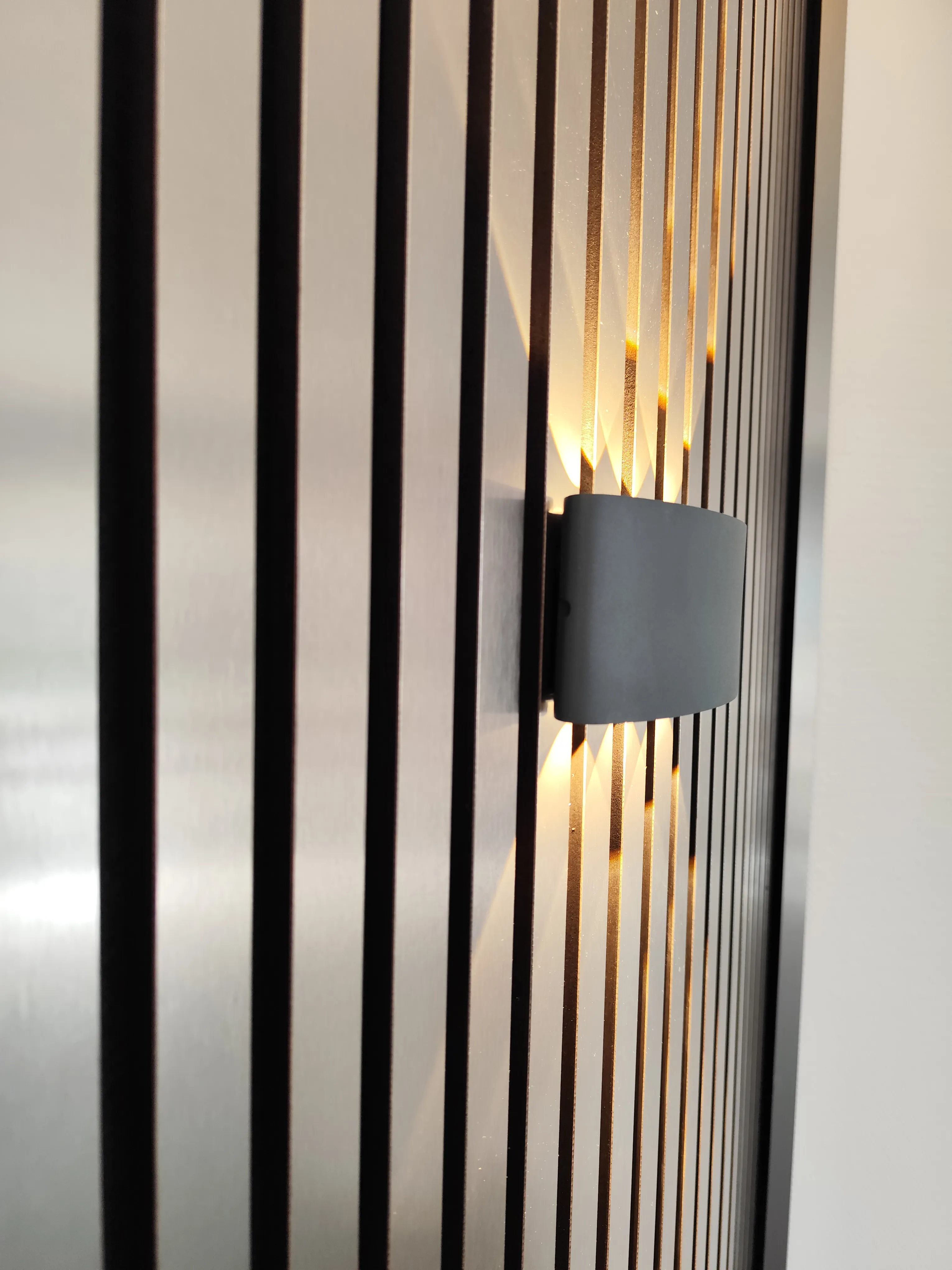 Detail einer Akustikpaneel Wand mit Wandleuchte und Holzlamellen